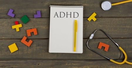 Mental health concept – text ADHD, attention deficit hyperactivity disorder, notepad, stethoscope, colorful jigsaw puzzle